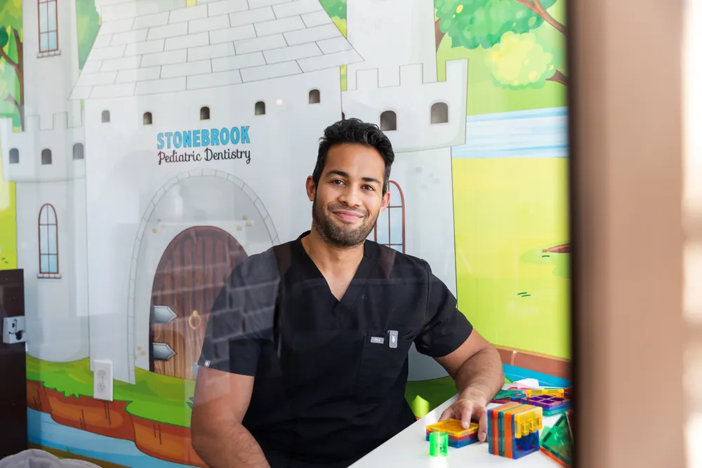 A smiling pediatric dentist in black scrubs in the castle-themed play area at Stonebrook Pediatric Dentistry